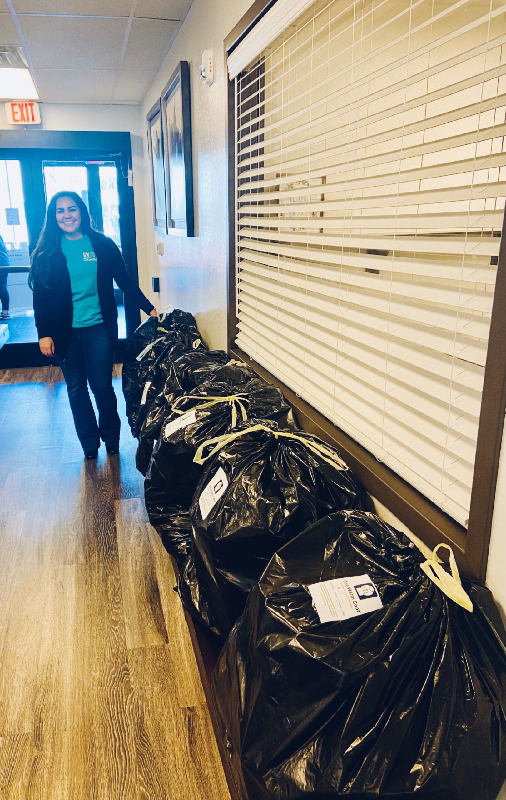 A woman stands in a hallway with a trail of bags filled with donated coats.