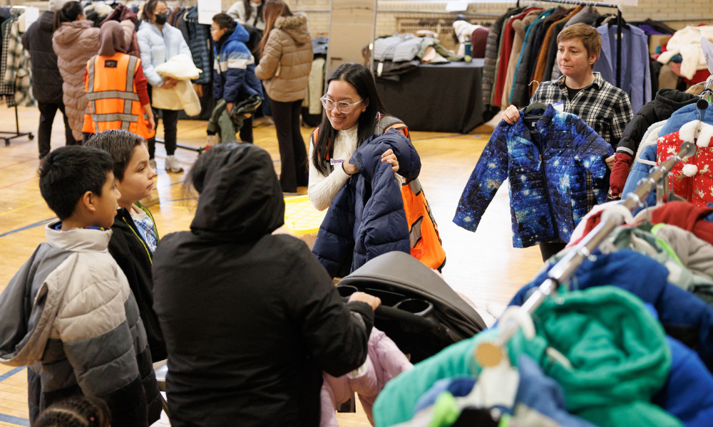 People are distributing winter coats in a community setting, suggesting a nonprofit partnership.