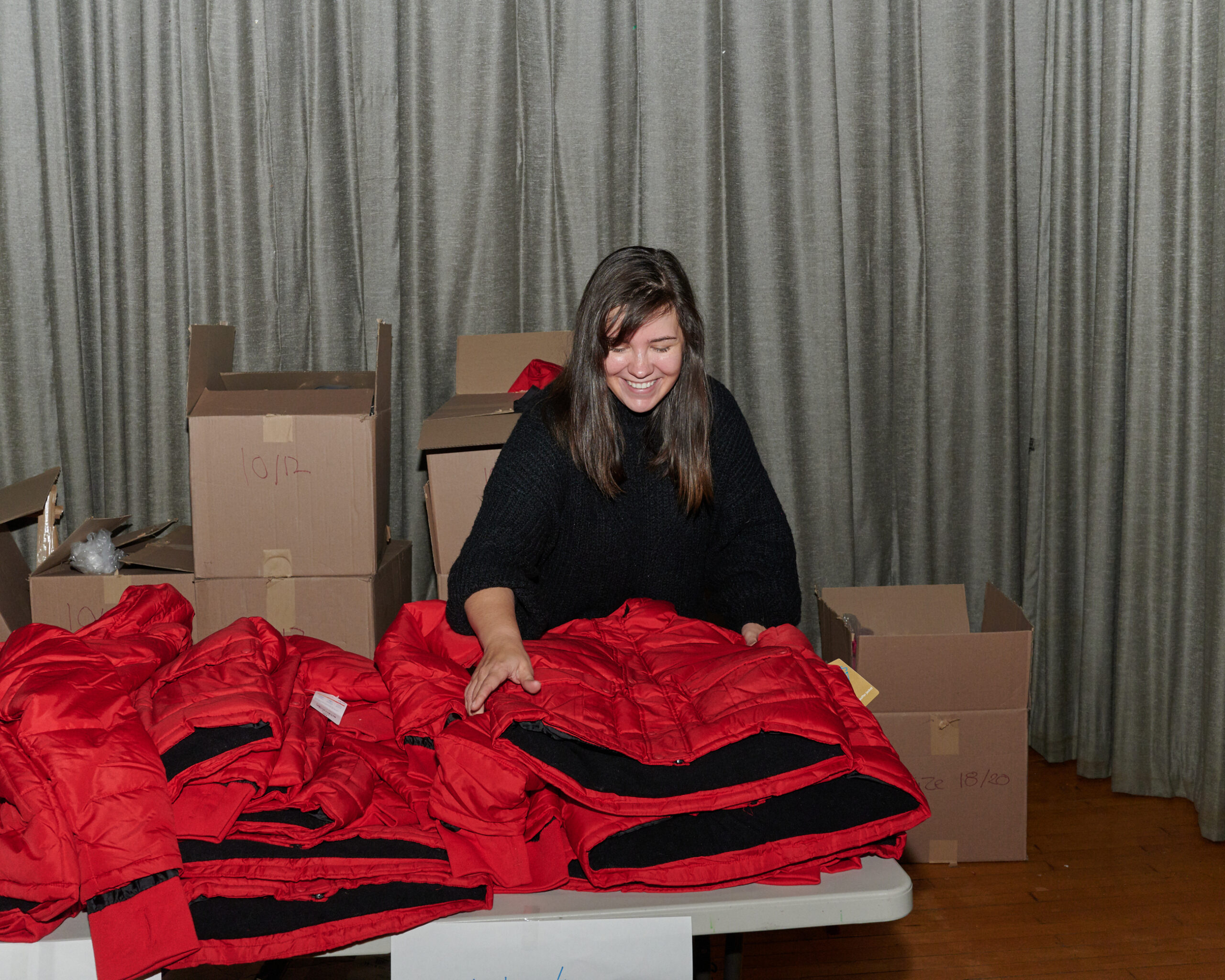 A woman with dark hair organizes a pile of red coats for a coat distribution 