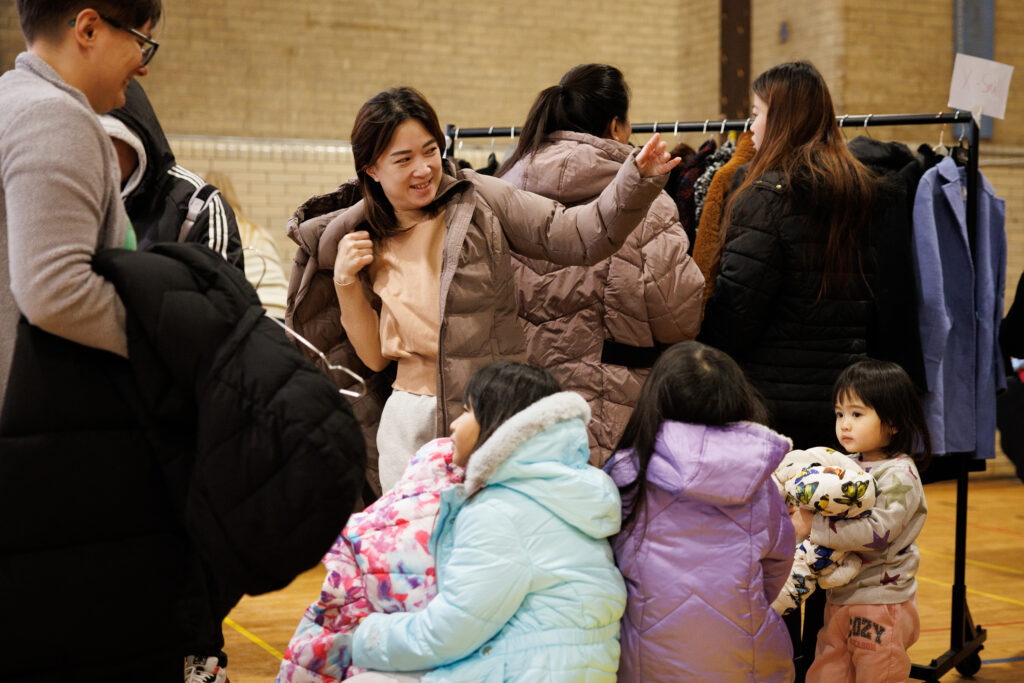 People are browsing and trying on coats, likely participating in a coat distribution event. 