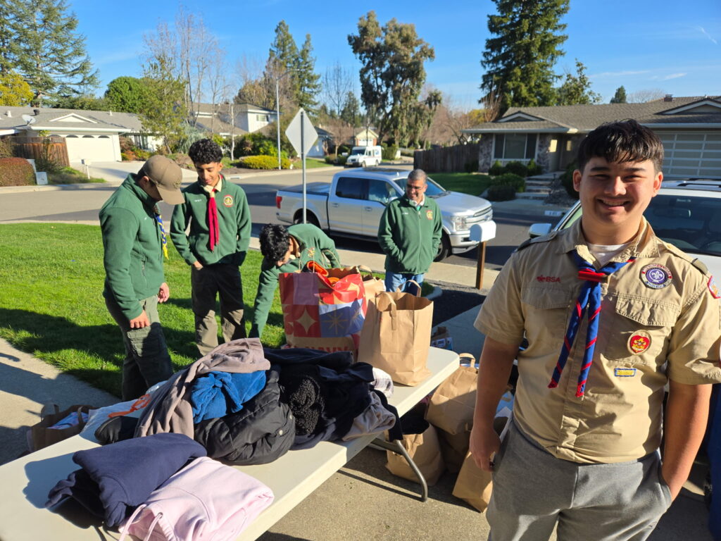A group of scouts is organizing clothes on tables in a suburban area, likely participating in a community service or donation event.